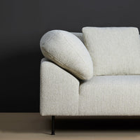 Light gray textured sofa with a round arm cushion against a dark gray backdrop. Modern minimalist design.