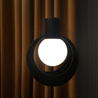 Black circular pendant light with a white globe, contrasting against warm brown curtains. Modern and minimalist design.
