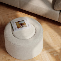 Round cream ottoman with textured fabric on a wooden herringbone floor, featuring a circular top and seamless design.