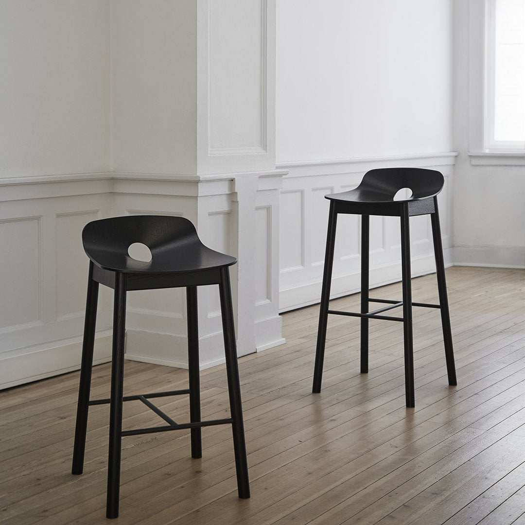 Black modern bar stools with smooth curves and minimalistic design, set against a light wooden floor and bright white walls.
