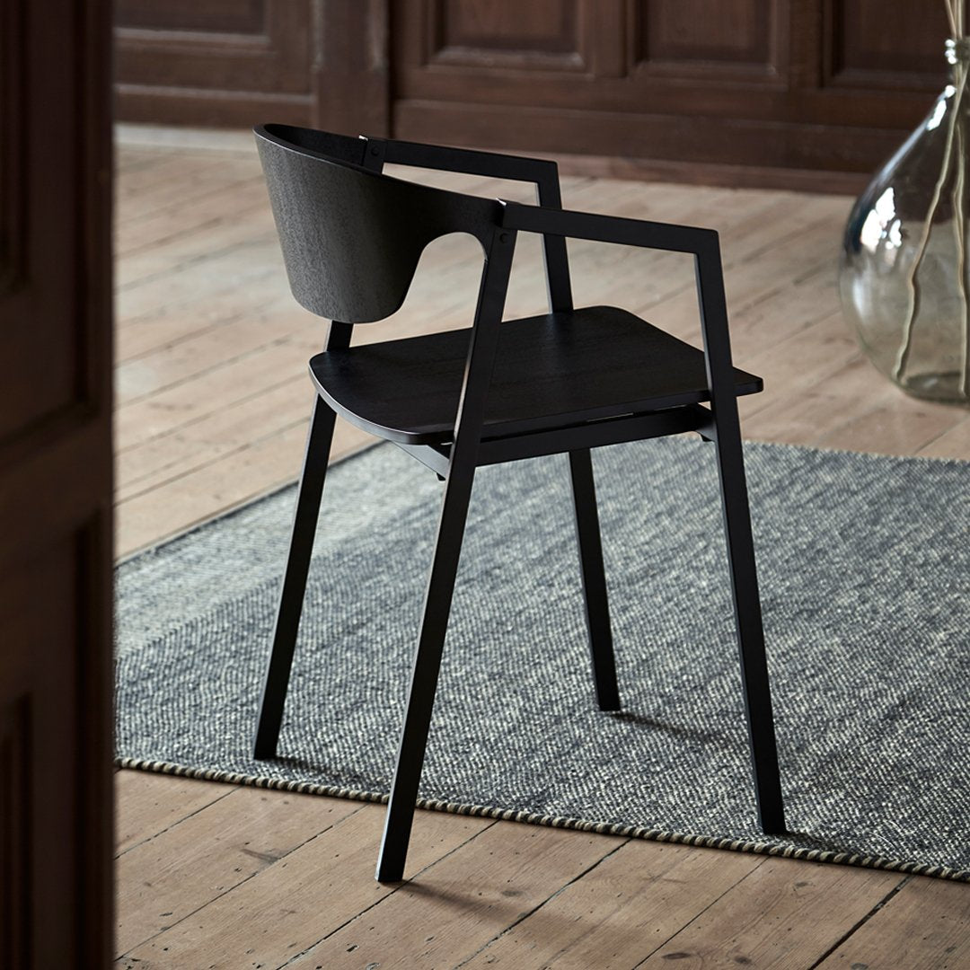 Black minimalist chair on a textured gray rug, showcasing sleek lines and contrasting materials.