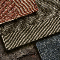 Textured fabric swatches in rust red, olive green, and deep navy, showcasing unique patterns and weaves.