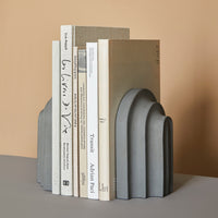 Gray sculptural bookends with arch patterns, set against a soft beige background.