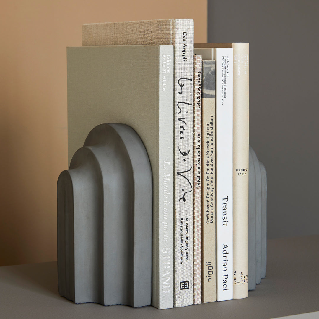 Gray textured bookend with curved arches, featuring neutral green and beige shades, styled with stacked white books.