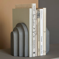 Gray textured bookend with curved arches, featuring neutral green and beige shades, styled with stacked white books.