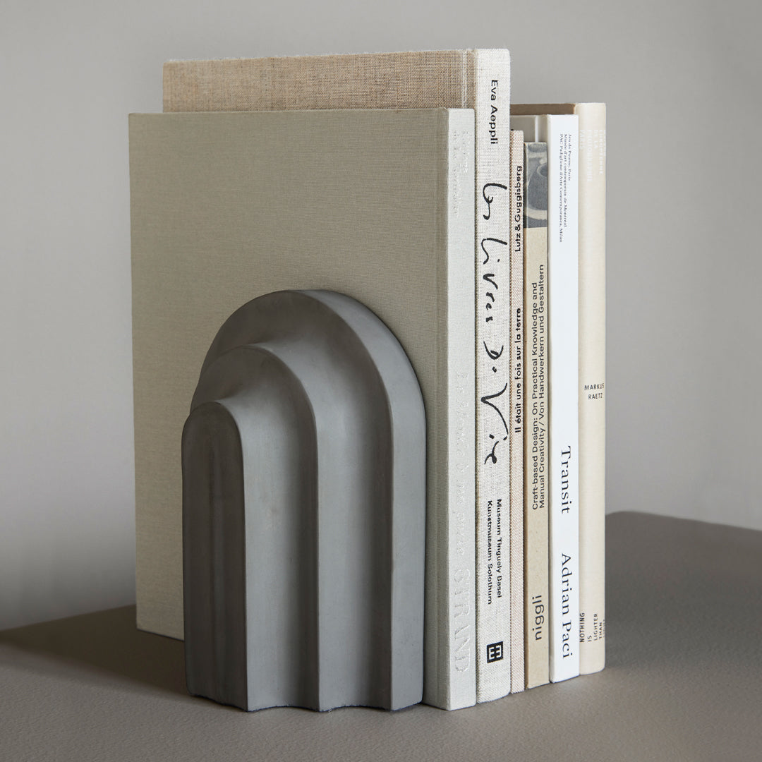 Gray curved bookend with smooth arches, complemented by neutral-colored books and a subtle beige backdrop.