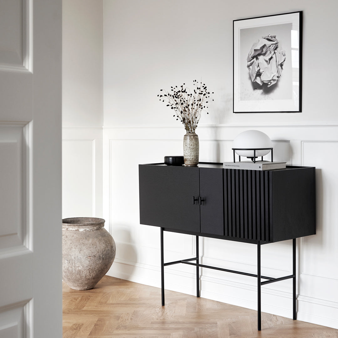 Sleek black cabinet with vertical ribbed pattern, set against a light wall with wooden flooring.