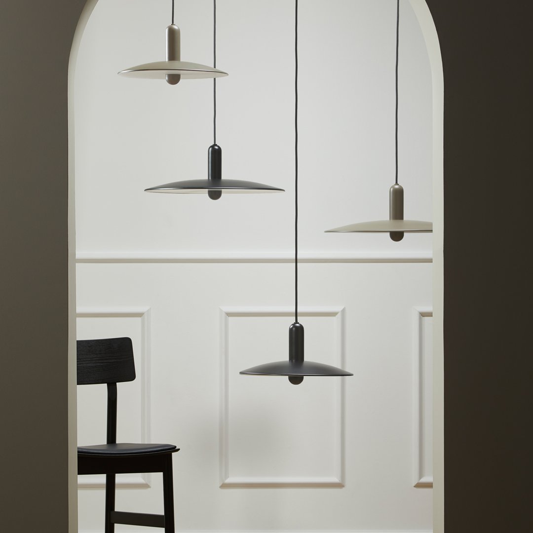 Three pendant lights in gray, beige, and black hang against a white wall with an arched doorway and a black chair.