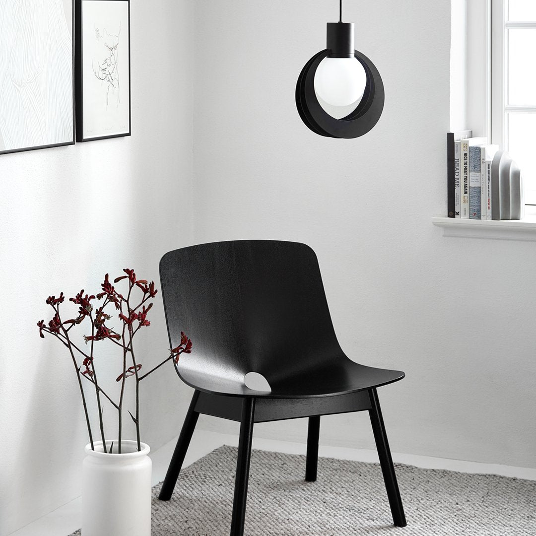 Black modern chair, white pendant light, and minimalist decor in a gray carpeted room with natural light.