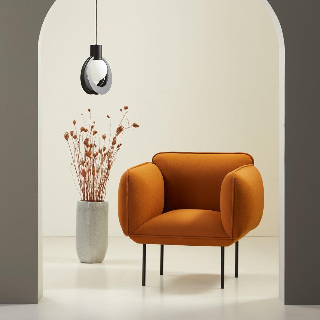 Orange upholstered chair with rounded arms, set against a neutral background and accented by simple decor.