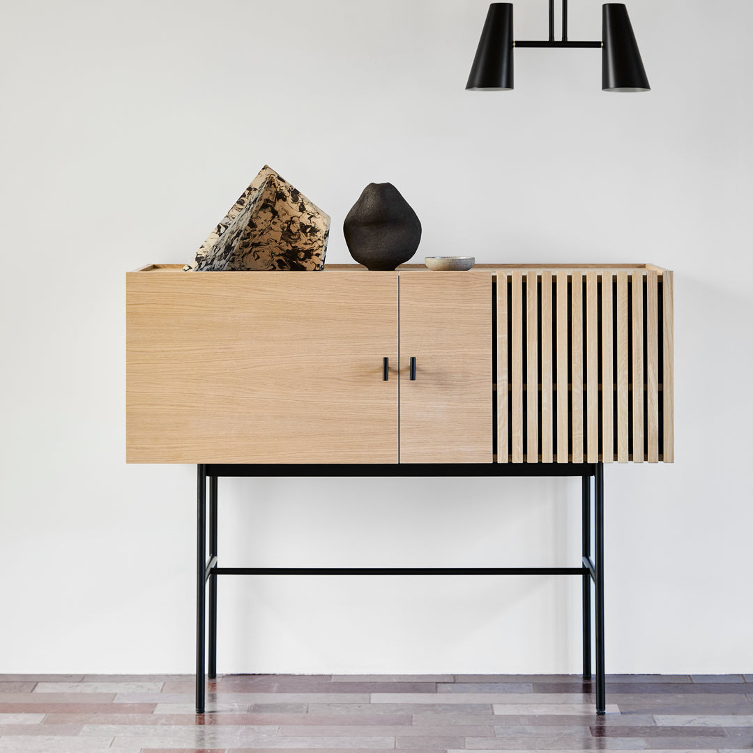 Light wood cabinet with vertical slats and a sleek black metal base, featuring natural textures and modern design.