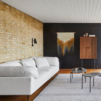 "Modern white sofa against textured brick and dark walls, complemented by a geometric wall hanging and a soft gray rug."