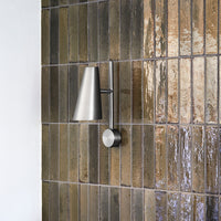 Modern wall lamp with a sleek silver finish against textured brown and glossy dark tile patterns.