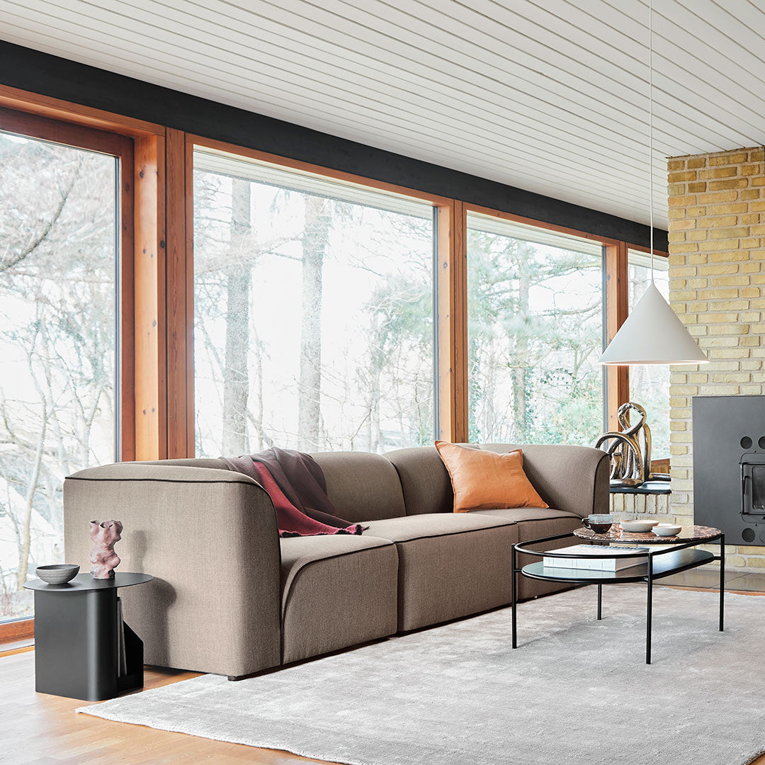"Modern beige sofa with orange and burgundy accents, set in a bright, minimalist living space with large windows."
