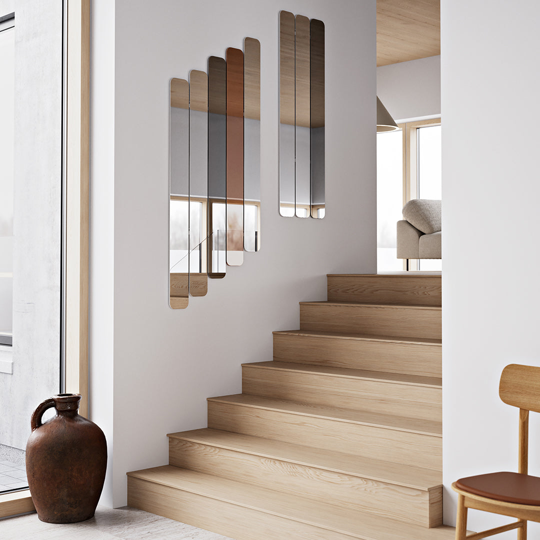 Reflective mirror panels in muted silver and bronze hues, set against a light wood staircase and white walls.