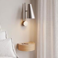 Modern silver wall lamp against a neutral wall, paired with a light wood shelf and soft white curtains.