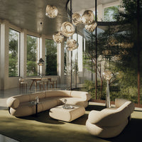 Beige curved sofa set on a green rug, with glass pendant lights, bright natural light, and lush greenery in the background.