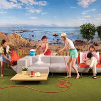 "Modern gray outdoor sofa with vibrant orange and green accents, set against a beach backdrop."