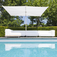 White sectional outdoor sofa under a large white umbrella beside a clear blue pool, surrounded by lush green landscape.