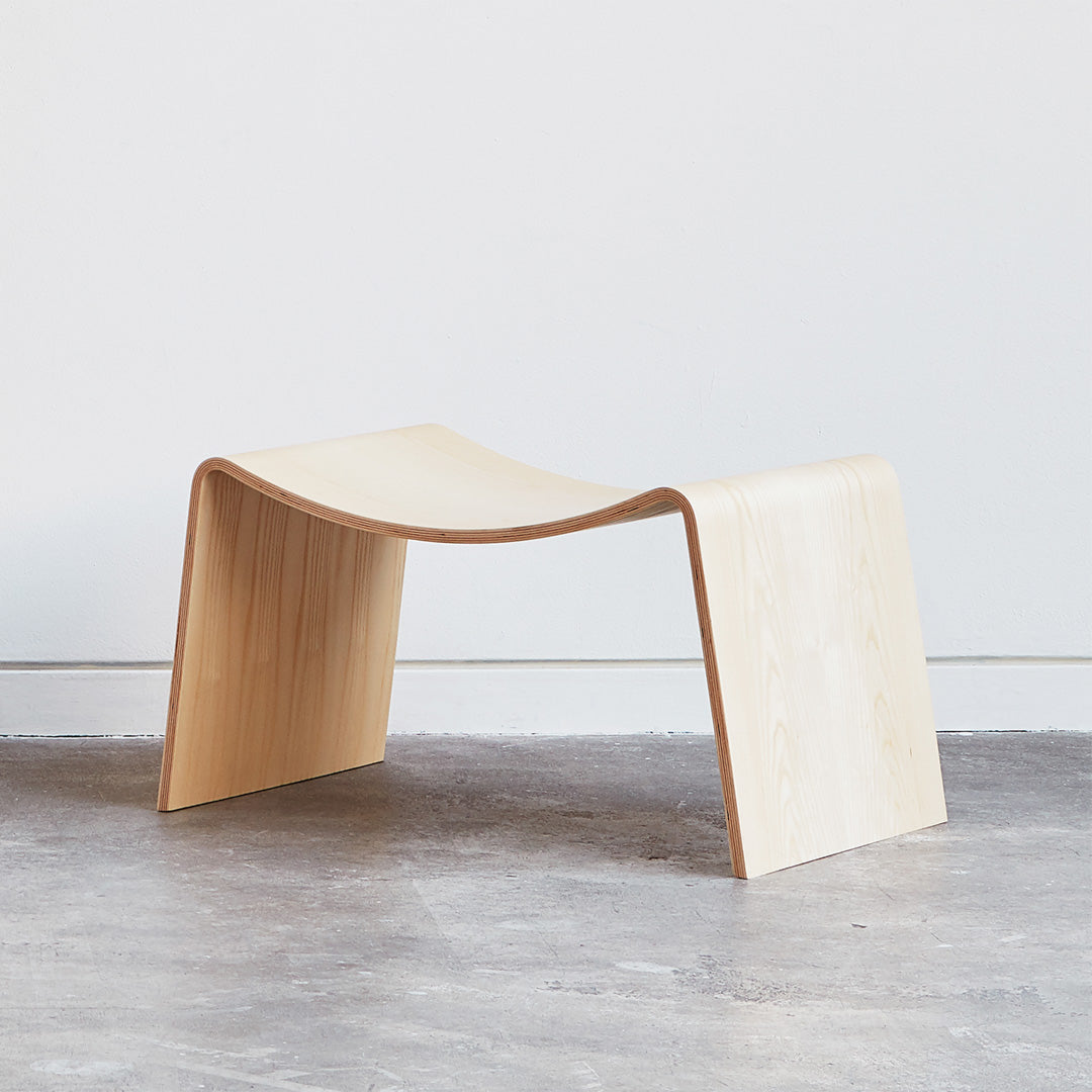 Curved light wood bench with smooth, natural finish and minimalist design against a neutral background.