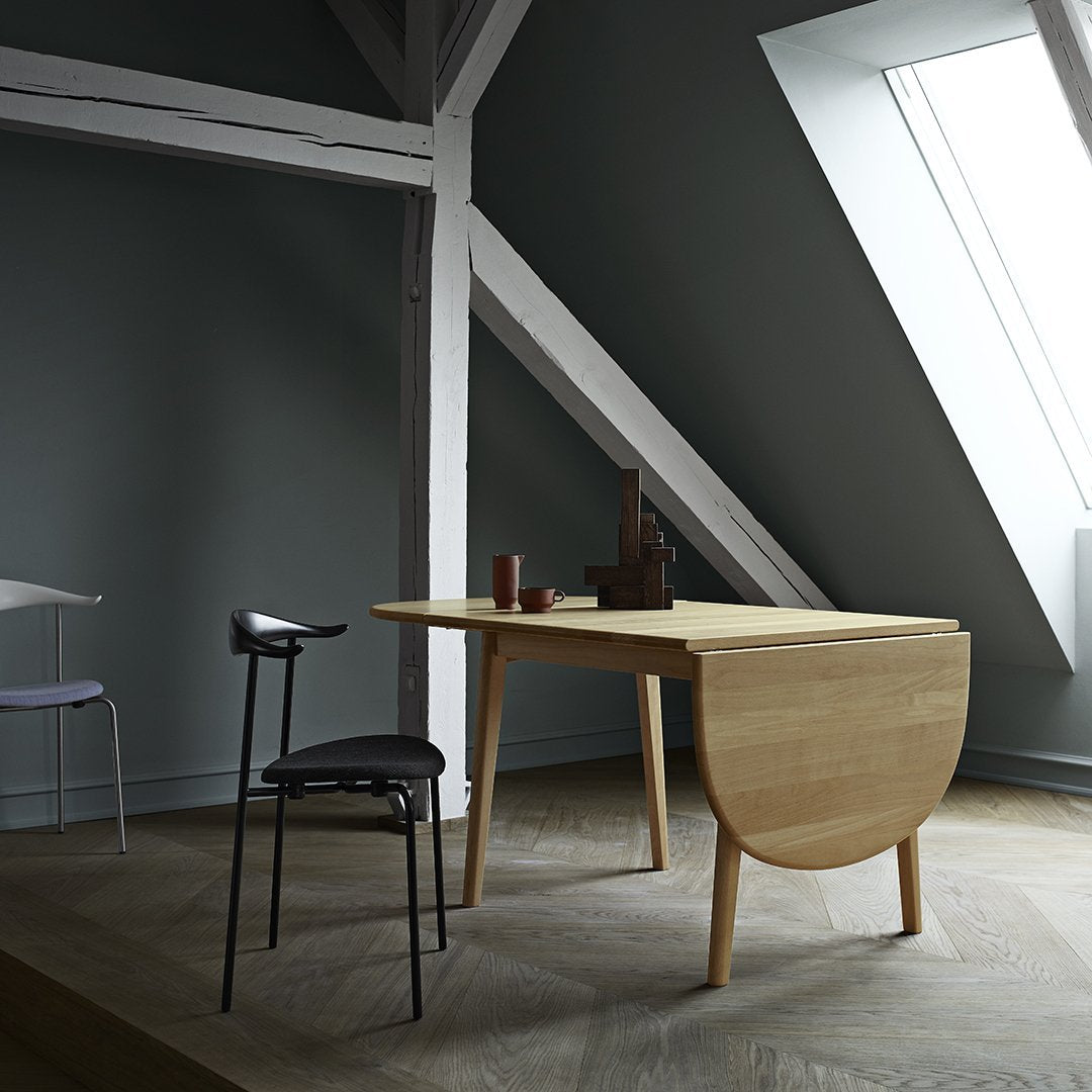 Modern wooden desk with a light oak finish, set against dark gray walls and a herringbone-patterned floor.