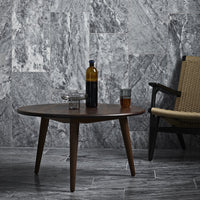 Round wooden coffee table with a dark brown finish, set against a textured gray marble wall and sleek gray floor tiles.