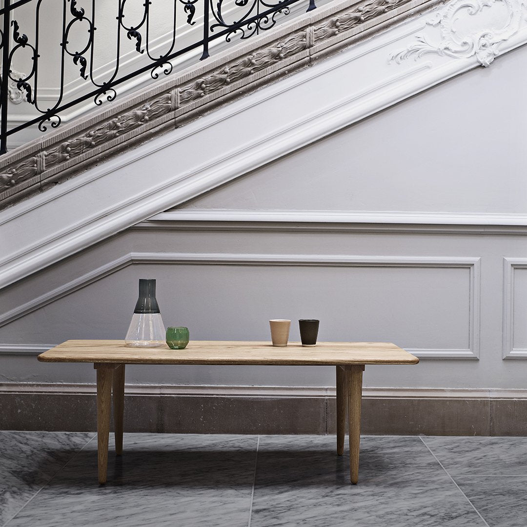 Natural wood table with beige surface, featuring green, clear, and dark brown decorative vases on a marble floor backdrop.