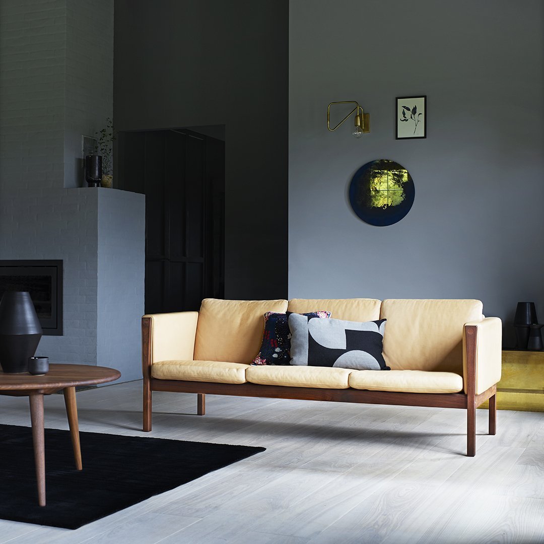 Modern beige sofa with abstract black and white patterned pillows, set against muted gray walls and light wood flooring.
