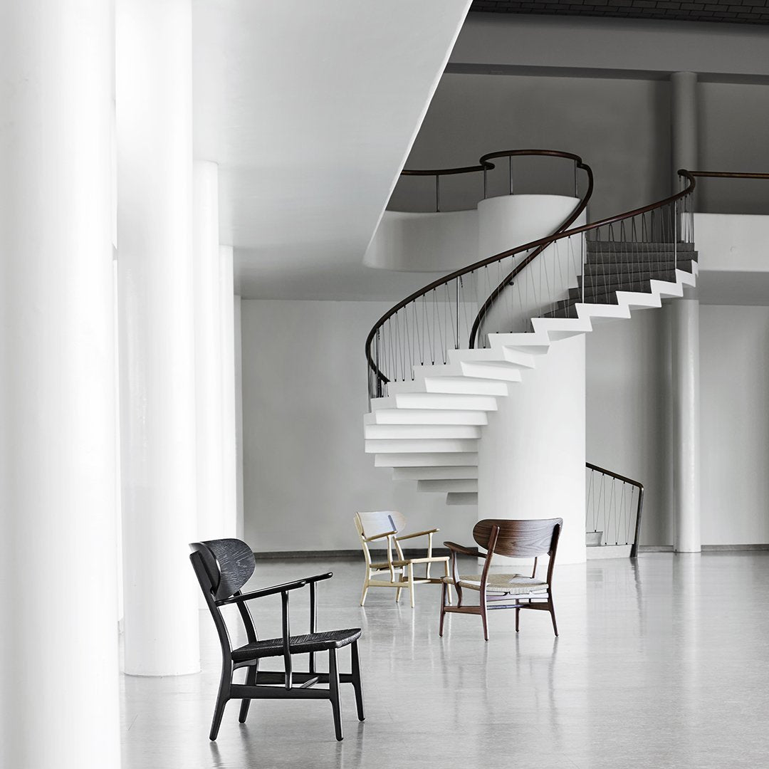"Contemporary chairs in black, natural wood, and white, set against a minimalist gray interior with a spiral staircase."