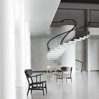 "Contemporary chairs in black, natural wood, and white, set against a minimalist gray interior with a spiral staircase."