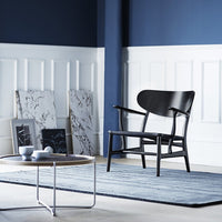Stylish black chair against a navy and white backdrop with a striped blue rug, featuring marble-patterned artwork.