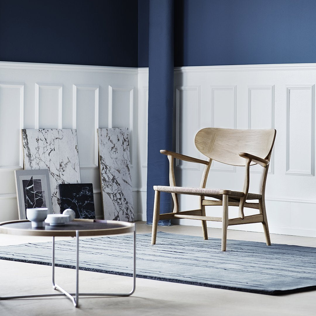 Light oak chair on a blue rug, paired with white marble decor against a navy wall. Modern minimalistic colors and textures.