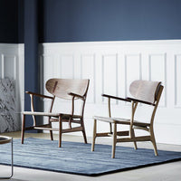 Two wooden chairs in walnut and light oak, paired with a textured blue rug against a white paneled wall.