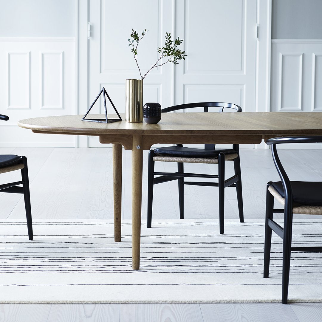 Light wood table with black chairs, featuring a neutral striped rug and minimalist decor in a bright, airy space.