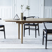 Light wood table with black chairs, featuring a neutral striped rug and minimalist decor in a bright, airy space.