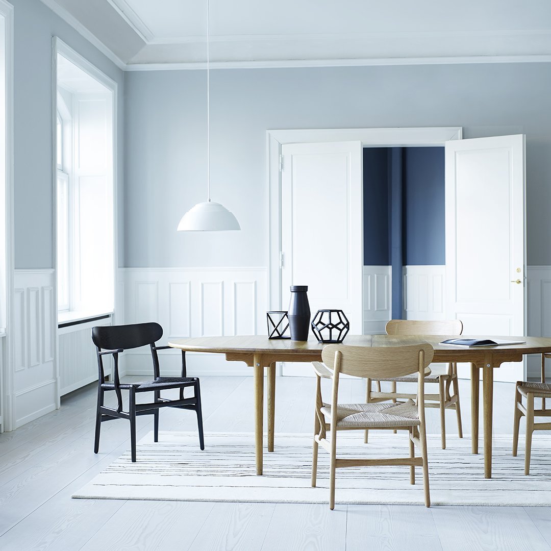Modern dining room featuring a light blue wall, white furniture, and a mix of black and wooden chair designs.
