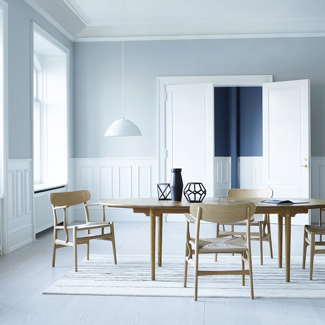 Light blue walls and white trim, paired with a natural wood table and chairs on a striped rug for a fresh, modern look.