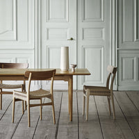Light wood table and chairs with woven seats, set against a soft mint green wall and white paneled doors.