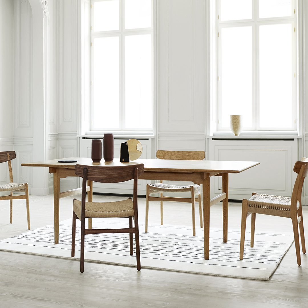 Light wood dining table with natural finish, complemented by beige and white patterned rug and minimalist decor.