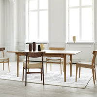 Light wood dining table with natural finish, complemented by beige and white patterned rug and minimalist decor.