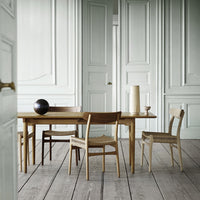 Wooden dining table with natural tones, featuring woven and solid chairs in light brown, dark brown, and off-white.