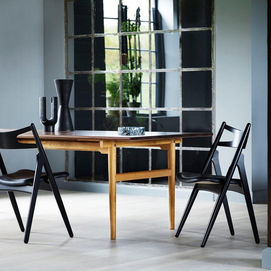 Elegant wooden dining table with natural oak finish, paired with sleek black chairs against a neutral backdrop.