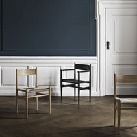Modern wooden chairs in natural wood and sleek black, set against a dark blue wall and herringbone floor pattern.