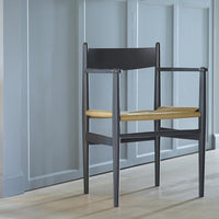 Black wooden chair with a natural woven seat against a light gray wall. Modern minimalist design.