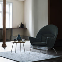 Dark teal chair on a light gray rug, featuring a minimalist wooden table and subtle lighting. Ideal for modern decor.