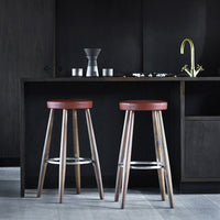 "Styled wooden bar stools with warm red seats and natural wood legs against a sleek dark backdrop."