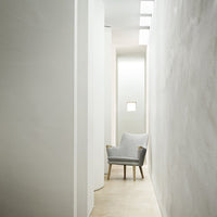 Light gray armchair with wooden legs in a minimalist white hallway. Soft textures and clean lines create a serene ambiance.