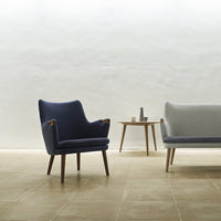 "Modern armchair in deep navy blue with wooden legs, paired with a light gray sofa, set against a minimalist backdrop."