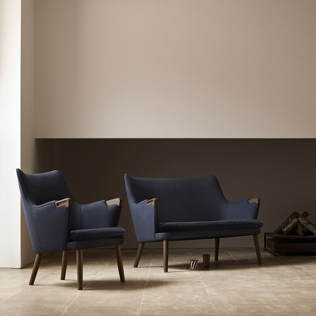 Navy blue upholstered sofa and armchair with wooden accents against a minimalist beige wall and floor.