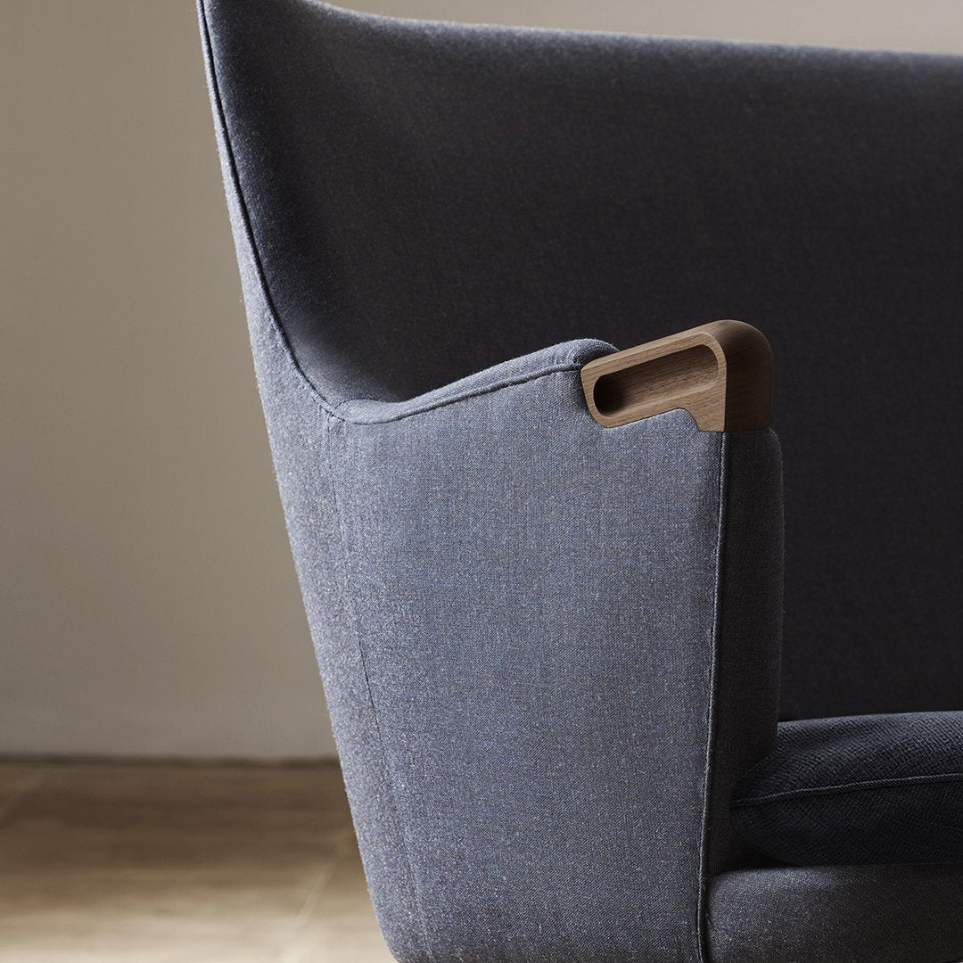 "Close-up of a modern chair in soft gray fabric with a sleek wooden armrest detail."